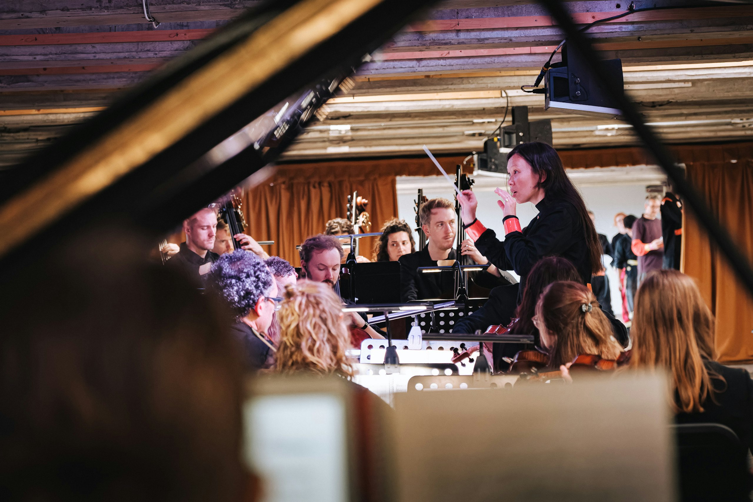 Garland, at Bold Tendencies: A conductor gestures to an orchestra, seen through the raised lid of a grand piano.